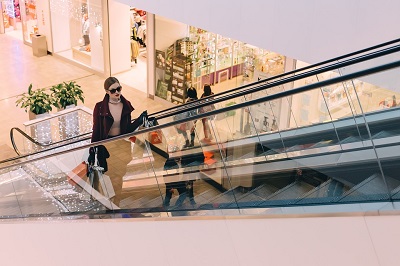 Woman riding mall escalator with full shopping bags