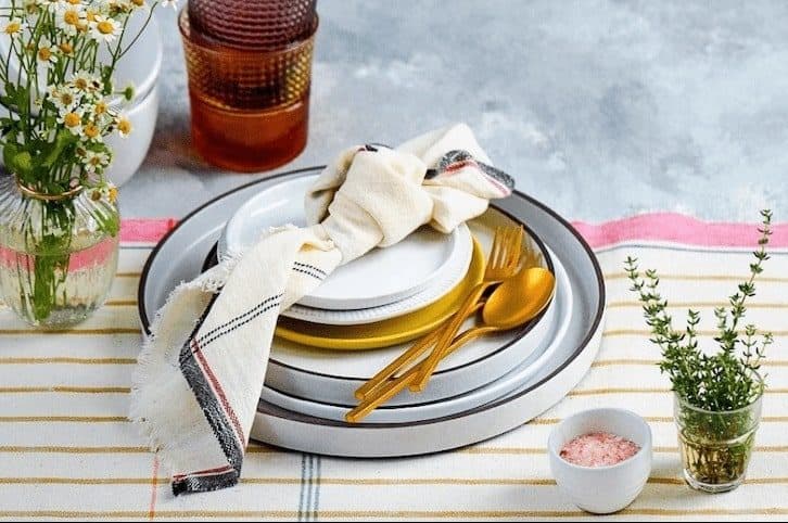 dinnerware with golden cutlery on a white and mustard striped tablecloth