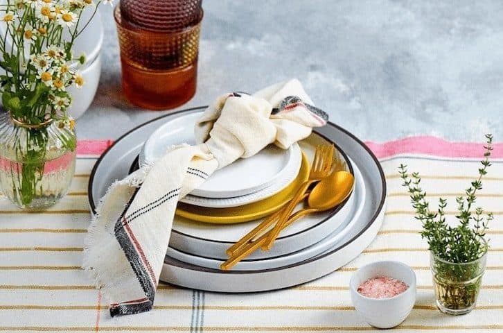 dinnerware with golden cutlery on a white and mustard striped tablecloth